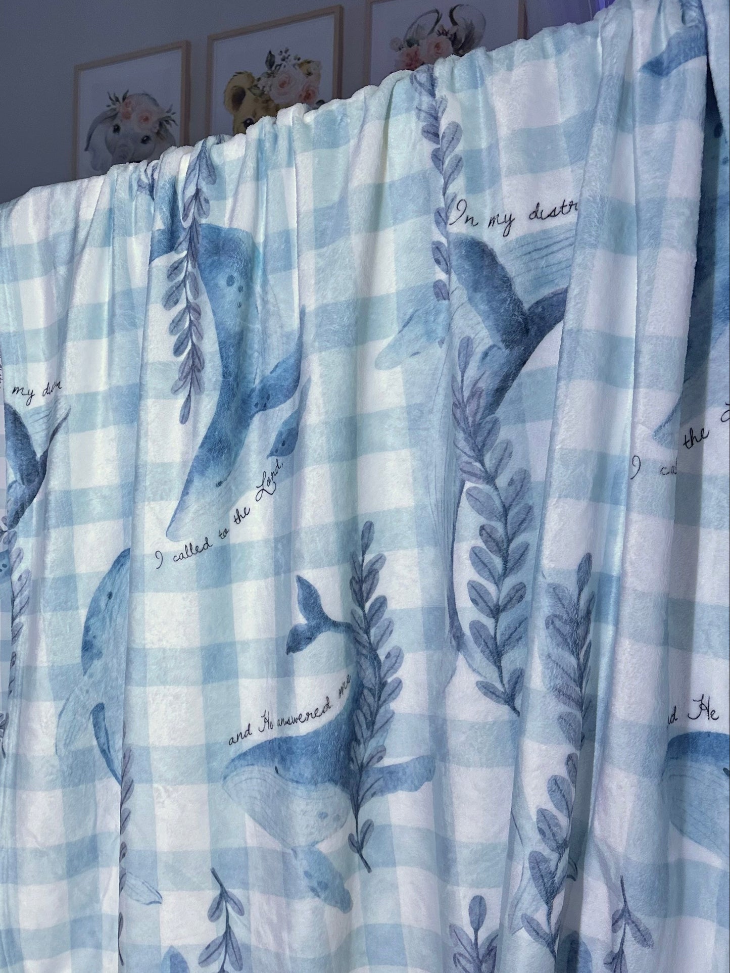 Baby crib with blue and white checkered sheet and whale pattern in a room.