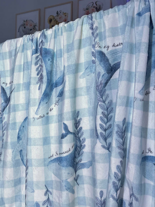 Baby crib with blue and white checkered sheet and whale pattern in a room.